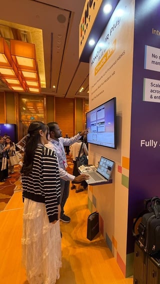 Attendee interacting with a HONO AI HR plugin demo on a screen while a representative explains features at a conference booth.