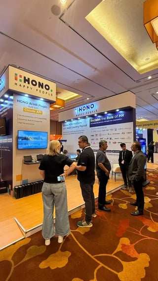 HONO booth at a tech conference with attendees discussing HR solutions in front of branded displays.