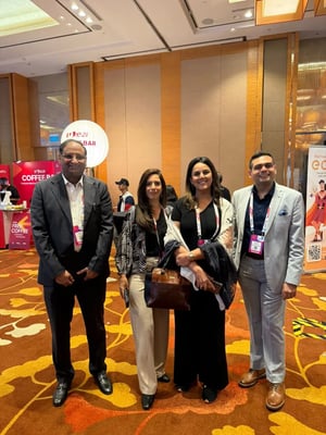Mukul with two conference attendees posing for a photo in a networking area with event branding in the background.